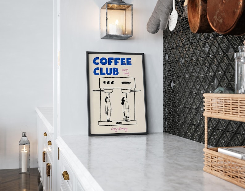 May include: A black framed poster with white text that reads 'COFFEE CLUB Served Daily Every Morning' and a black and white illustration of a coffee maker with two people standing underneath it.