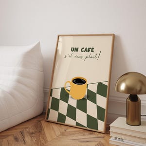 May include: A framed print with a yellow coffee cup on a black and white chequered background. The text on the print reads "UN CAF&Eacute; s'il vous pla&icirc;t!"