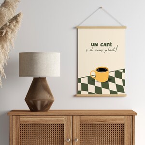 May include: A printable wall art design featuring a yellow coffee cup with black coffee on a black and white chequered background. The text reads "Un caf&eacute; s'il vous pla&icirc;t!"