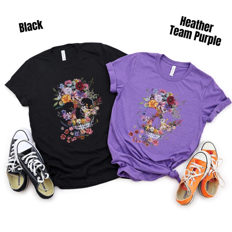 Pu&ograve; includere: Due magliette, una nera e una viola, con un design a teschio floreale. La maglietta nera ha scarpe da ginnastica bianche e nere, e quella viola ha scarpe da ginnastica arancioni. Il testo "Black" e "Heather Team Purple" &egrave; visibile.