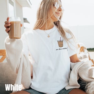 May include: White t-shirt with a graphic of a coffee cup with ice and a straw. The text "on the rocks" is below the cup.