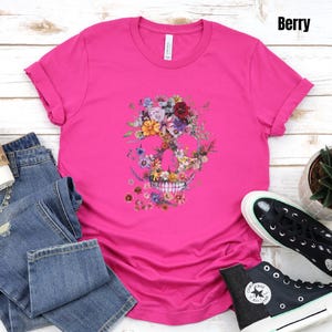Pu&ograve; includere: Una maglietta rosa acceso con un design a teschio floreale. Il teschio &egrave; composto da vari fiori colorati. La maglietta &egrave; abbinata a jeans blu e scarpe da ginnastica nere. La parola "Berry" &egrave; visibile nell'angolo in alto a destra.