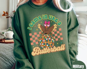 May include: A military green sweatshirt with the text "I came in like a Butterball". The graphic features a turkey wearing sunglasses and a bow, perched on a disco ball, set against a checkered background.