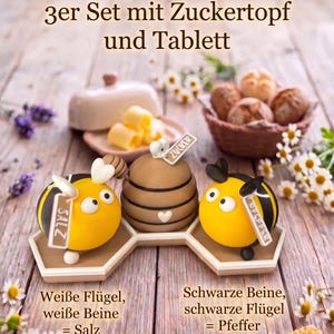 Könnte beinhalten: Ein dekoratives Servier-Set mit Zuckerdose, Tablett und Salz- und Pfefferstreuern. Die Salz- und Pfefferstreuer sind als gelb-schwarze Bienen gestaltet. Die Zuckerdose ist braun. Das Set enthält eine Butterdose und einen Korb mit Brötchen.