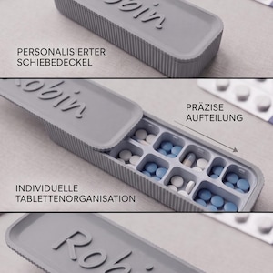 Könnte beinhalten: Ein grauer Pillenorganizer mit dem Namen "Robin" auf dem Deckel. Der Organizer ist geöffnet und zeigt Fächer mit blauen und weißen Pillen. Der Text auf dem Bild lautet "Personalisierter Schiebedeckel", "Präzise Aufteilung" und "Individuelle Tablettenorganisation".