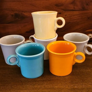 Puede incluir: Seis tazas de cerámica en diferentes colores, incluyendo amarillo, gris, azul y naranja. Las tazas tienen un diseño simple con una asa redondeada.
