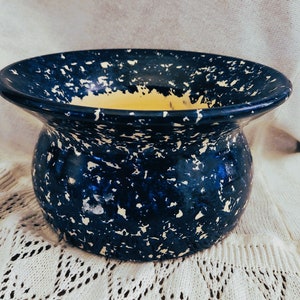 May include: A blue and white speckled ceramic planter with a yellow interior. The planter has a wide rim and a rounded body.