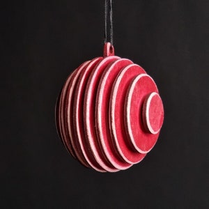 Puede incluir: Un adorno navideño rojo y blanco a rayas colgando de una cuerda sobre un fondo negro.