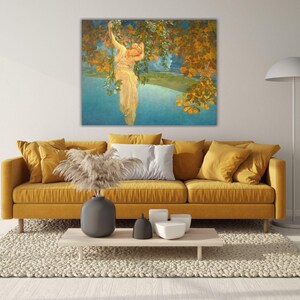 May include: A large framed art print depicts a woman in a flowing gown reaching for golden leaves. The artwork hangs above a mustard yellow sofa with matching throw pillows. A light-colored rug and a modern coffee table complete the living room setting.