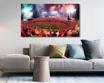May include: A rectangular wall art print depicting a crowded football stadium filled with spectators wearing red, surrounding a green field. Above the stadium, vibrant fireworks in shades of red, white, and blue illuminate the night sky with smoke.