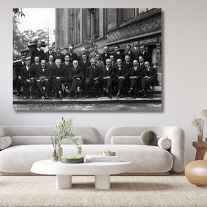 May include: A black and white wall art print featuring a large group of men in formal suits and ties posing for a photograph in front of a stone building. The group is arranged in two rows, with some seated and others standing behind them.