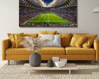 May include: A rectangular wall art print depicting a large stadium at night with a bright green football pitch, illuminated stands filled with spectators, and fireworks exploding in the sky above the roof structure, displayed in a living room.