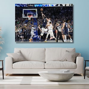 May include: A rectangular canvas print depicting a professional basketball game in progress. Players in dark blue and white uniforms are on the court near the hoop. A scoreboard at the top displays game statistics, and a crowd fills the background.