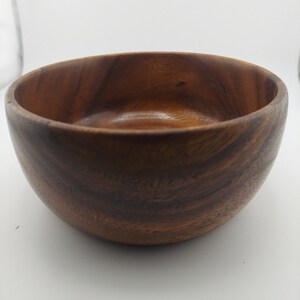 May include: A dark brown wooden bowl with a smooth, rounded interior. The bowl is made of natural wood and has a rustic, handcrafted look.