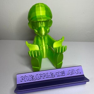 May include: A lime green 3D printed figurine of a video game character with a purple base that reads "Pineapple Fog 420".