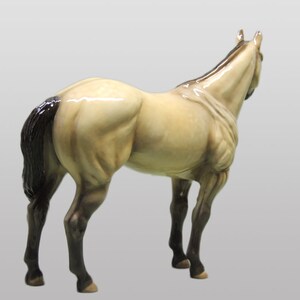 May include: A ceramic figurine of a horse with a light brown body, black mane and tail, and black legs. The horse is standing on a white background.