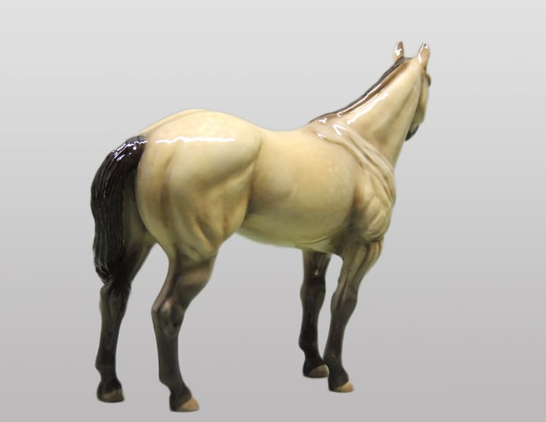 May include: A ceramic figurine of a horse with a light brown body, black mane and tail, and black legs. The horse is standing on a white background.