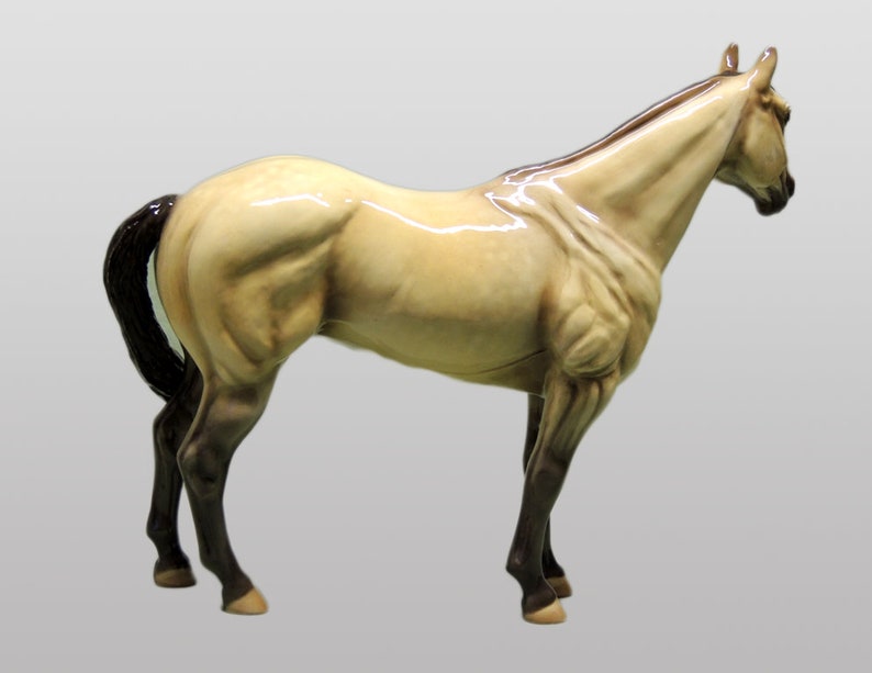 May include: A ceramic figurine of a horse in a light brown color with a black mane and tail. The horse is standing on all four legs with its head turned to the side.