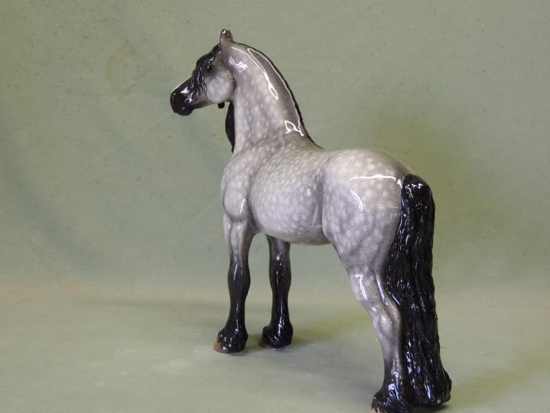 Puede incluir: Una figurita de caballo de porcelana gris y blanca moteada con una crin y cola negras. El caballo est&aacute; de pie con la cabeza girada hacia un lado.