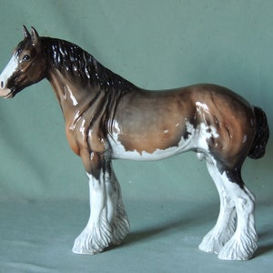May include: A brown and white painted ceramic horse figurine with a black mane and tail. The horse is standing on all four legs with its head turned to the left.