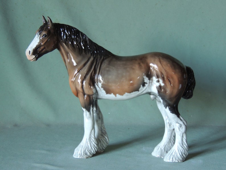 May include: A brown and white painted ceramic horse figurine with a black mane and tail. The horse is standing on all four legs with its head turned to the left.