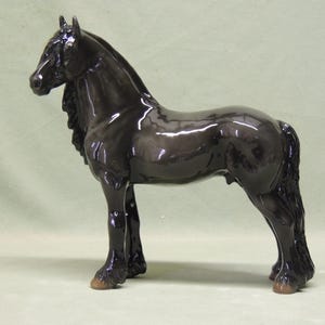 Op de afbeelding: Een zwart porseleinen beeldje van een paard met een lange, vloeiende manen en staart. Het paard staat met zijn hoofd hoog en zijn benen licht gebogen.