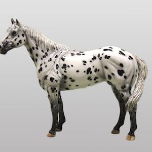Op de afbeelding: Een porseleinen beeldje van een wit en zwart gevlekt paard. Het paard staat met zijn hoofd naar links gedraaid.