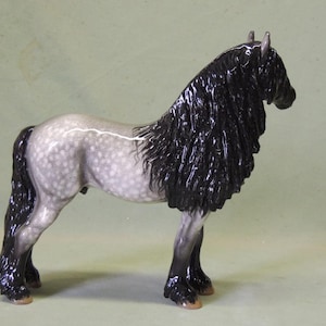 Puede incluir: Una figurita de porcelana gris y blanca de un caballo con una larga melena y cola negras. El caballo est&aacute; de pie sobre sus cuatro patas y tiene una larga melena y cola fluidas.