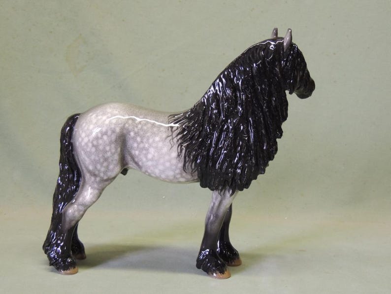 Puede incluir: Una figurita de porcelana gris y blanca de un caballo con una larga melena y cola negras. El caballo est&aacute; de pie sobre sus cuatro patas y tiene una larga melena y cola fluidas.