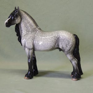 Puede incluir: Una figurita de porcelana gris y blanca de un caballo con una crin y cola negras. El caballo est&aacute; de pie sobre sus cuatro patas con la cabeza en alto.