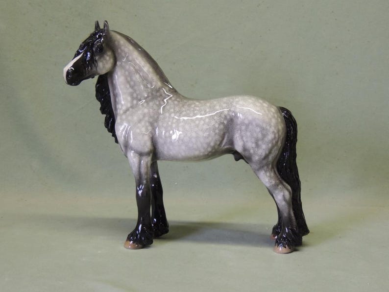 Puede incluir: Una figurita de porcelana gris y blanca de un caballo con una crin y cola negras. El caballo est&aacute; de pie sobre sus cuatro patas con la cabeza en alto.