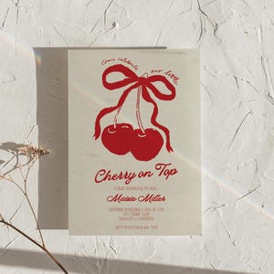 May include: A baby shower invitation with a red cherry illustration and the text "Come celebrate our little Cherry on Top, A Baby Sprinkle Honoring Maisie Miller, Saturday November 3, 2023 at 2 PM, 123 Cherry Lane, Sausalito, California, RSVP to Lucy 123-456-7890".