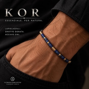 Könnte beinhalten: Ein Armband aus zylindrischen, abwechselnd blauen Lapislazuli-Perlen und goldfarbenen Hämatit-Abstandshaltern. Der Text KOR ESSENZIALE, PER NATURA, LAPISLAZZULI, EMATITE DORATA, ACCIAIO 316L und NEROSCARLATTO HANDMADE JEWELS ist im Bild zu sehen.