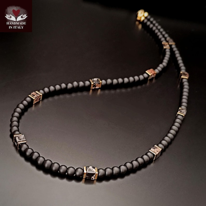 K&ouml;nnte beinhalten: Eine schwarze Perlenkette mit goldfarbenen quadratischen Akzenten. Die Halskette hat kleine, runde schwarze Perlen und mehrere quadratische Perlen mit einem Muster. Handgefertigt in Italien.