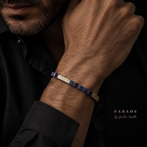 Può includere: Un bracciale con segmenti alternati di perline quadrate blu profondo e sottili barre metalliche dorate striate. Il testo FARAOS by Giulia Torelli è stampato nell'angolo in basso a destra dell'immagine su uno sfondo scuro.