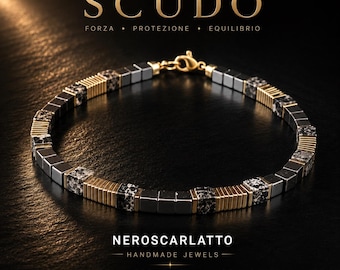 May include: A bracelet featuring alternating segments of metallic gray cube beads, gold-toned ribbed cylindrical spacers, and speckled black and white stone cubes. The piece includes a gold-toned lobster clasp closure and displays the text SCUDO and NEROSCARLATTO.