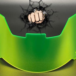 May include: A neon green football helmet visor with a curved, semi-transparent design. Above the visor, a graphic illustration depicts a fist punching through a cracked, dark surface, creating a shattered effect with black lines and debris.