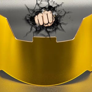 May include: A gold-tinted football helmet visor featuring a graphic of a fist punching through a cracked surface. The visor has a curved, semi-transparent design with mounting holes on the lower left and right sides for attachment to a helmet.