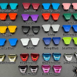 May include: A collection of 18 different colored plastic controller caps for a gaming console. The caps are arranged in rows and labeled with their color names, such as Dolphins Teal, Maroon, Powder Blue, Pink, Orange, Purple, Red, Green, Yellow, Black, Gray, Buffalo Blue, Lions Blue, White, Navy Blue, Seattle Green, Gold Chrome, Red Chrome, Blue Chrome, Silver Chrome, Gun Metal, and Pink Chrome.