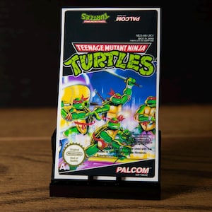 May include: A rectangular Teenage Mutant Ninja Turtles video game box for the Nintendo Entertainment System. The cover features the four turtles in action poses with red masks, the Palcom logo, and the official Nintendo Seal of Quality.