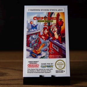 May include: A rectangular video game cartridge for the Nintendo Entertainment System featuring the title Chip 'n Dale Rescue Rangers 2. The label displays colourful cartoon characters on a city rooftop, the Capcom logo, and official Nintendo branding.