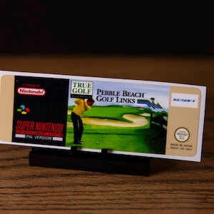 May include: A Super Nintendo game cartridge for "True Golf Pebble Beach Golf Links." The label shows a golfer, a golf course scene, and the Nintendo logo. The cartridge is a PAL version, made in Japan.