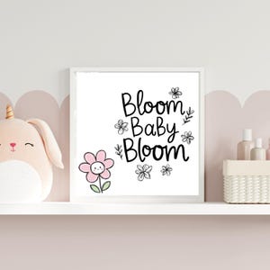 Puede incluir: Una impresi&oacute;n enmarcada en blanco con texto negro que dice "Bloom Baby Bloom" rodeada de peque&ntilde;as flores negras. Una flor rosa con una carita sonriente est&aacute; en la esquina inferior izquierda.