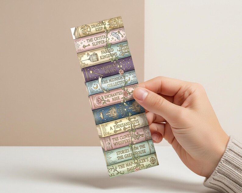 Op de afbeelding: Een bladwijzer met een stapel fantasyboeken met titels als "Dragons Keep" en "The Crystal Slipper". De bladwijzer heeft een bloemenrankontwerp en wordt door een hand tegen een neutrale achtergrond gehouden. De boekruggen zijn in pastelkleuren.