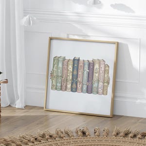 Op de afbeelding: Een ingelijste print met een verzameling boeken in vintage-stijl met bloemaccenten. De boeken zijn in verschillende kleuren, waaronder groen, roze, blauw en paars, en zijn in een rij gerangschikt. De lijst is goudkleurig.