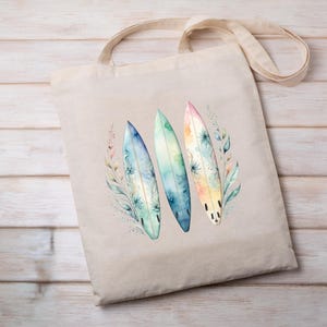 K&ouml;nnte beinhalten: Eine beige Tragetasche mit einem Aquarell-Design aus drei Surfboards mit floralen Akzenten. Die Surfboards sind in Blaut&ouml;nen, Gr&uuml;n- und Gelbt&ouml;nen bemalt.