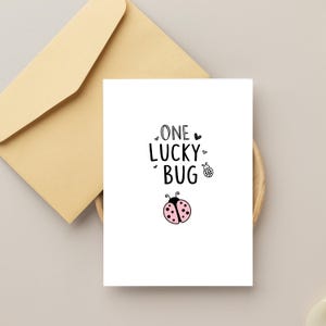 Puede incluir: Una tarjeta blanca con texto negro que dice "One Lucky Bug" con una ilustraci&oacute;n de mariquita rosa y negra.