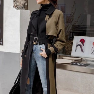 May include: A long black and green trench coat with a black belt and a black turtleneck underneath. The coat has a unique design with a black panel on the left side and a green panel on the right side.