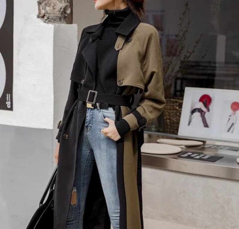 May include: A long black and green trench coat with a black belt and a black turtleneck underneath. The coat has a unique design with a black panel on the left side and a green panel on the right side.