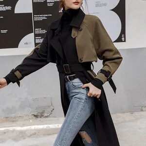 May include: A black and olive green trench coat with a belt. The coat has a double-breasted closure and a collar.